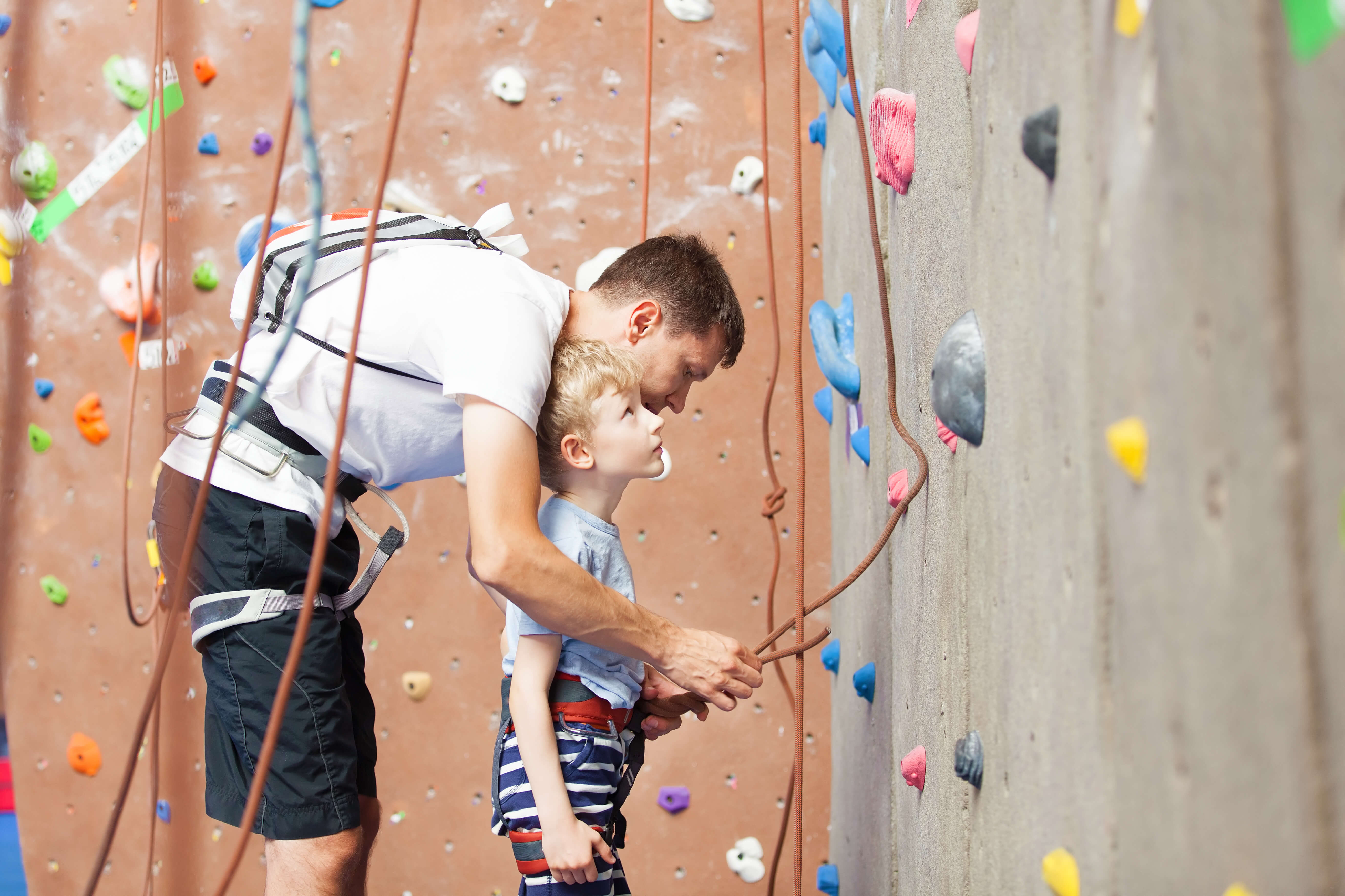 young father preparing his little son for climbing in indoor gym